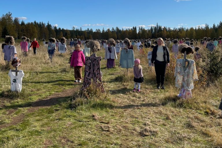 Lapset ja äiti kulkevat Hiljaisen kansan turvepäisten hahmojen keskellä Suomussalmella