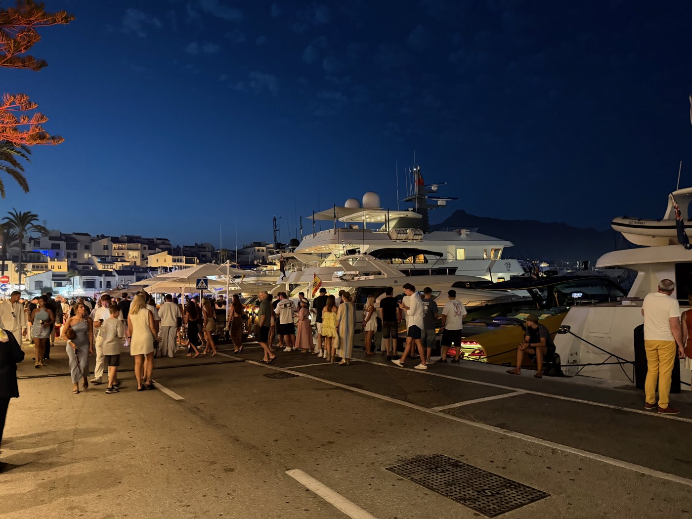 Puerto Banúsin satama iltavalaistuksessa, jahteja ja kävelijöitä laiturilla